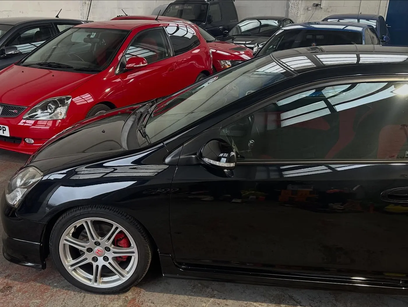 A black Civic Type R EP3 Premier Edition indoors, with a red EP3 and other cars behind it